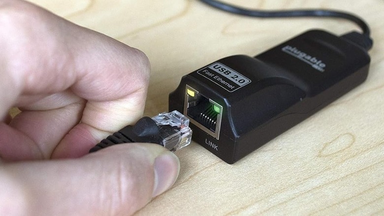 A person plugging in an Ethernet cable into a USB to Ethernet adapter