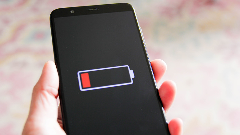 a hand holding an Android phone that has a low battery symbol