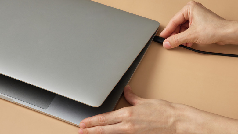A person connecting a charge cable to a laptop.