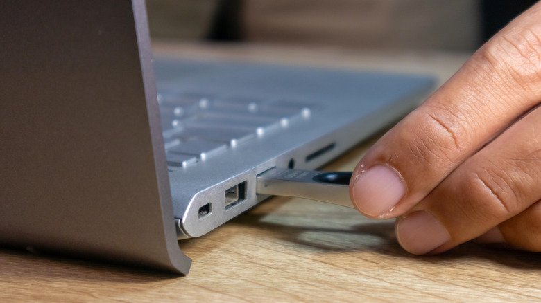 person inserting a flash drive into a laptop's USB port