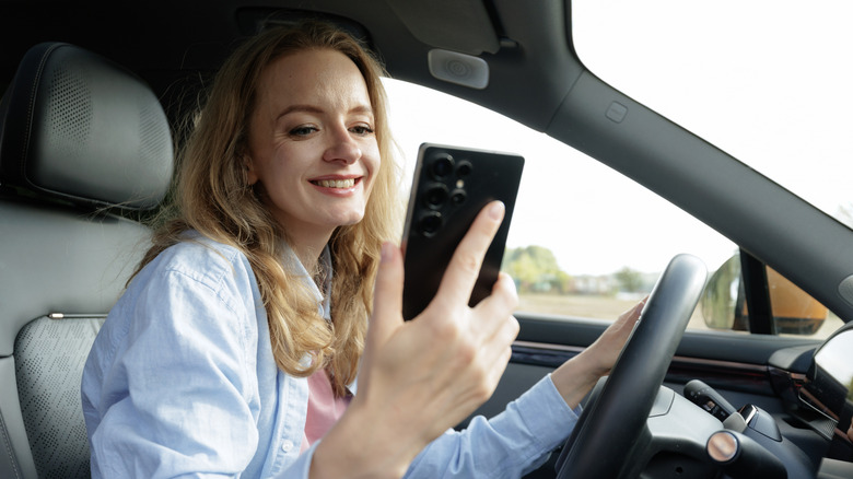 Lady holding phone for voice controls in car while one hand is on the wheel