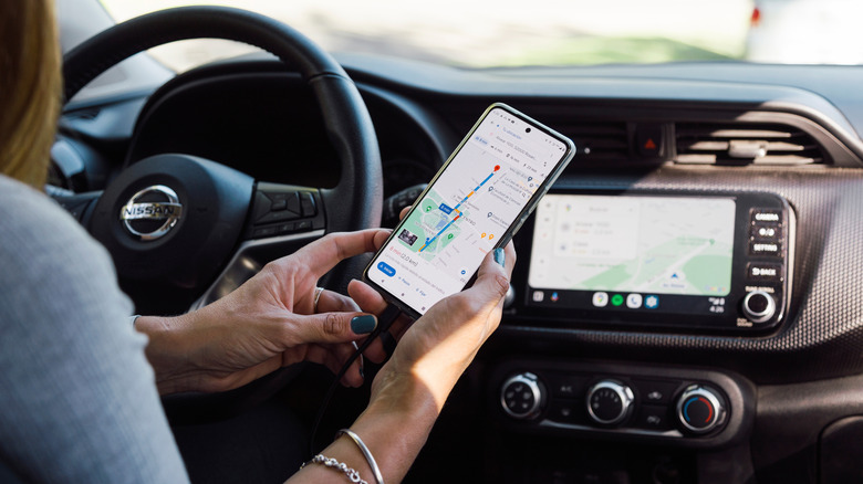 Woman holding phone in hand with Google Maps on screen, with infotainment system mirroring Maps