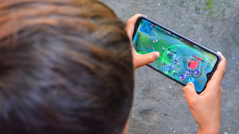 Child playing a mobile game on a smartphone outdoors.