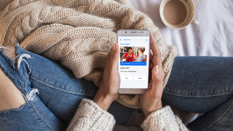 A person's hand on their legs, holding a phone while learning Spanish with Busuu