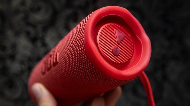 A person holding a red JBL Bluetooth speaker.