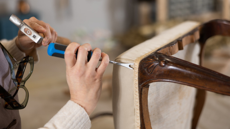 Man wearing blue apron adjusts the underside of a black office chair.