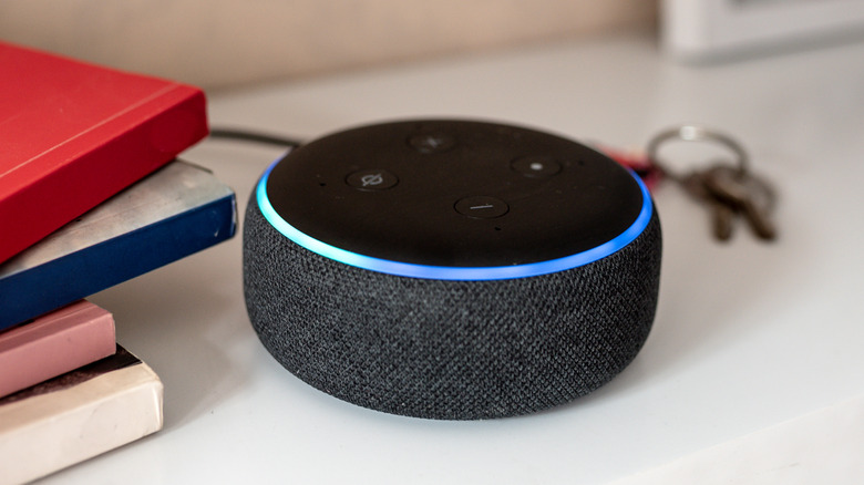 Amazon Echo smart speaker with a blue light ring beside books and keys on a table.