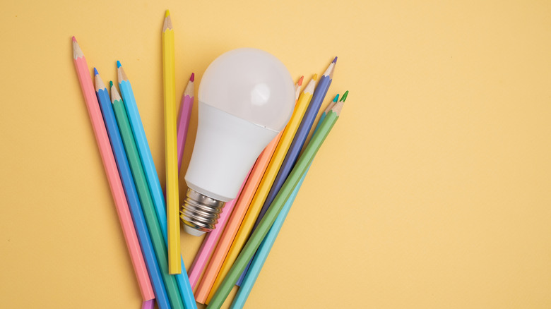 Light bulb on yellow background with colored pencils surrounding it.