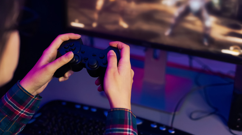 Person holding a generic game controller in front of a PC monitor and keyboard