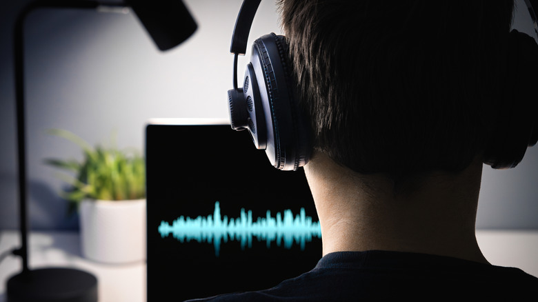A person listening to headphones while looking at a sound wave graphic on a computer screen