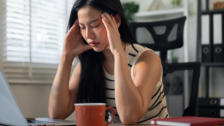 Woman at desk with a headache while looking at her laptop
