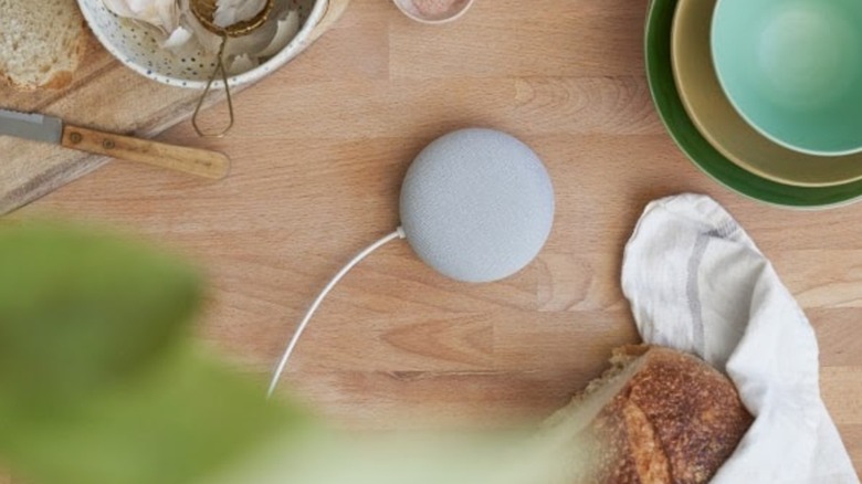 Google Nest Mini Speaker in white color on a wooden table surrounded by food and plates