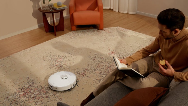 Person reading a book while RoboRock S8 MaxV Ultra robotic vacuum cleans a rug