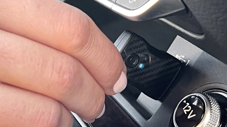 A person plugging an Aluratek wireless car adapter into their dashboard.
