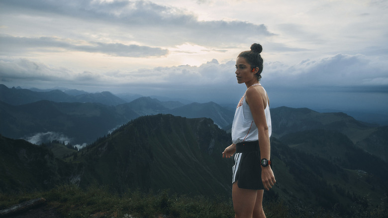 A person standing by the mountains wearing Suunto bone conduction headphones.