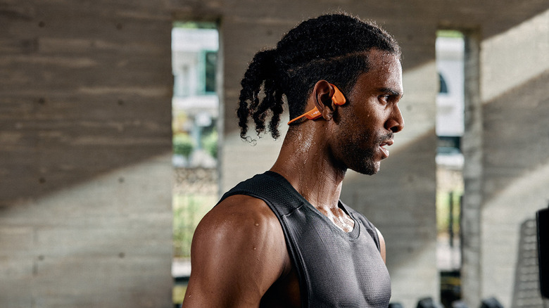 A person sweating while working out in a gym and wearing the Shokz OpenRun Pro bone conduction headphones.