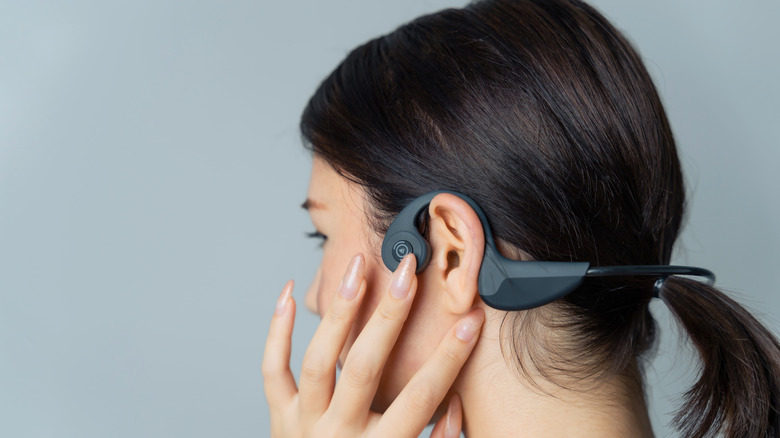 A person touching the bone conduction earphone they're wearing