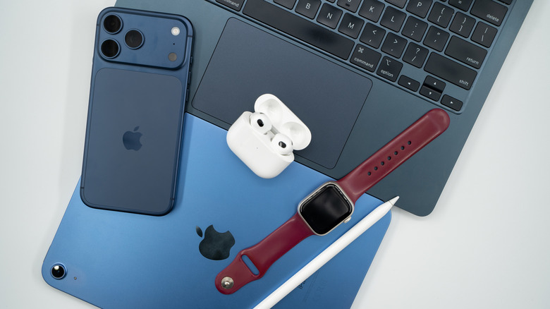Apple ecosystem devices including iPhone, iPad, MacBook, AirPods, and Apple Watch placed on a grey surface