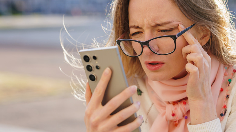 Person adjusting glasses and attempting to look at phone screen