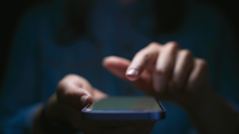 Close-up of hands using phone in dark setting indicating privacy