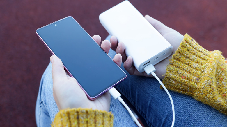 Close-up of a person holding a bulky power bank while charging a phone