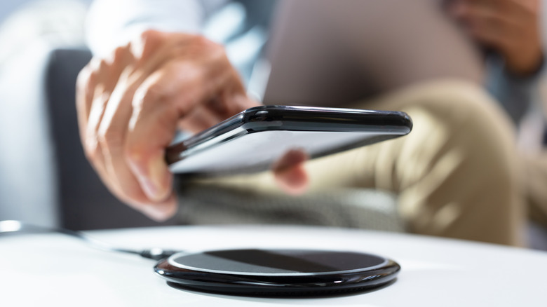 Close up of a hand holding a smartphone over a wireless charger