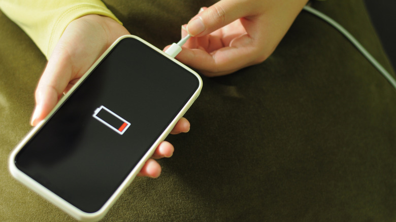 Close up of hands plugging a phone displaying a low battery symbol