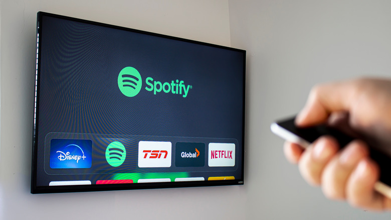 Hand holding remote pointing at TV on wall with Spotify logo on screen