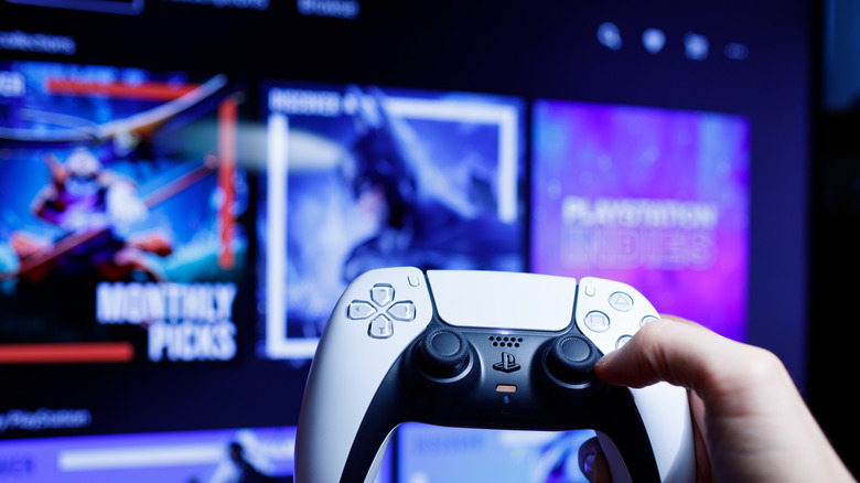 A person holding a DualSense controller in front of a TV showing the PlayStation Store.