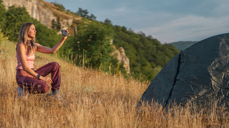 A woman taking a photo with her phone while camping