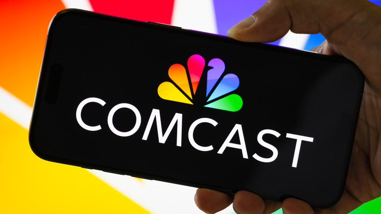 A person holding a smartphone displaying the logo of Comcast Corporation