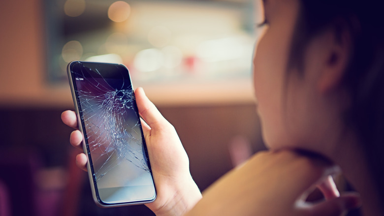 A woman looking at a cracked phone screen