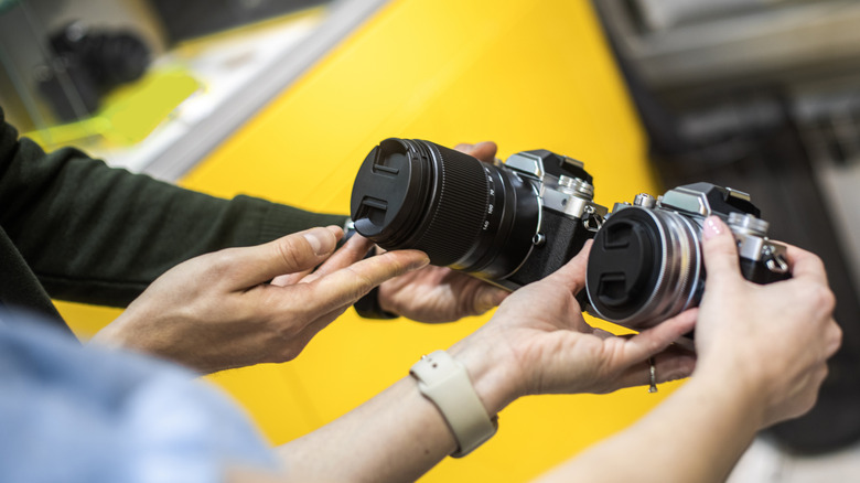 Close up on female's hands seen holding photo camera while salesman is helping her with the selection in a camera shop.