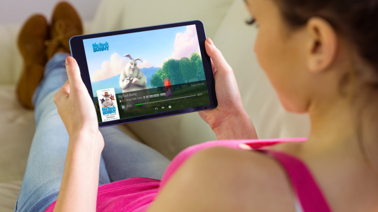 Person on laying on couch holding tablet watching movie with Emby