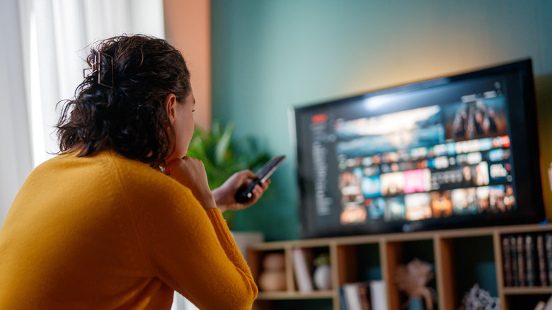 Person sitting with remote in hand pointed at TV on shelf