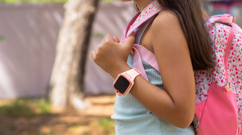 Young girl with a backpack and a pink smartwatch walking down the street.