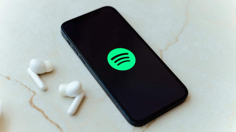 Spotify logo on a smartphone, a pair of earbuds on the table next to it