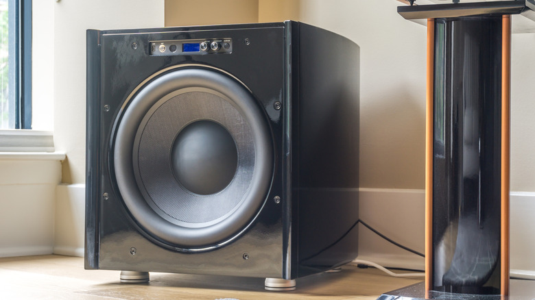 A home theater subwoofer sitting next to a speaker stand