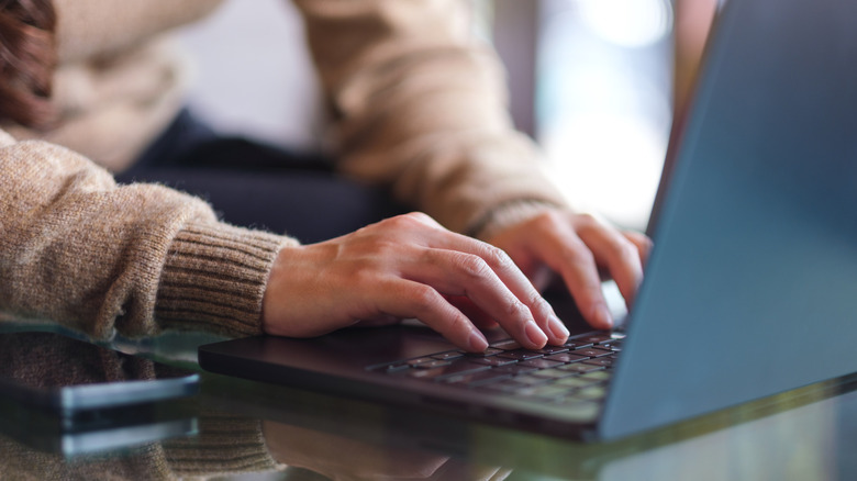 A close-up of a person's hands typing on a laptop