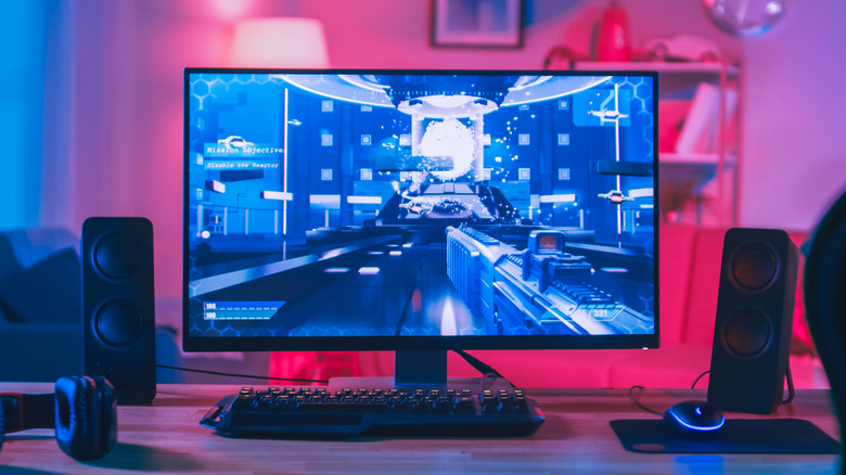 A computer gaming rig featuring a display showing a first person shooter, whereas a mouse, keyboard, and speakers are also present