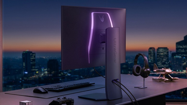 The LG UltraGear 32-inch OLED Dual Mode Gaming Monitor sits on a desk in front of a large city skyline, there's also a mouse, keyboard, and gaming controller on the desk
