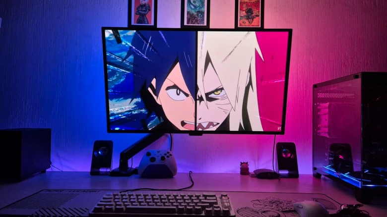 A Samsung 27-inch Odyssey OLED G5 QD-OLED Gaming Monitor sits at a computer desk as it displays a still from an anime, there is RGB lighting surrounding the monitor, and a computer tower also sits next to it