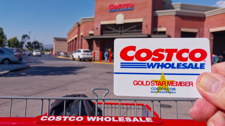 A hand holding a Costco membership card in front of a store.