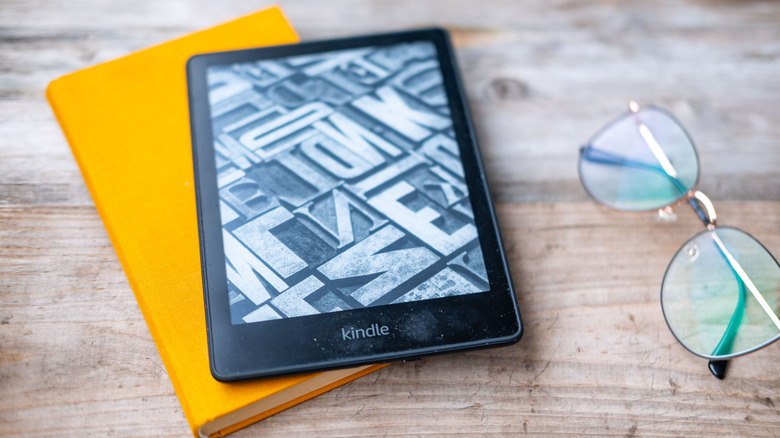 Modern Kindle reader on a book with glasses nearby.