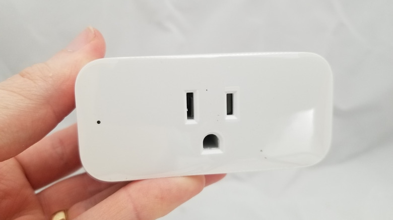 A person holding a run-of-the-mill-looking, rectangular smart plug.