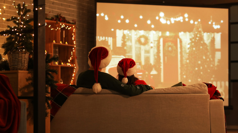 Two people watching a Christmas film on a projector screen in a living room decorated for Christmas