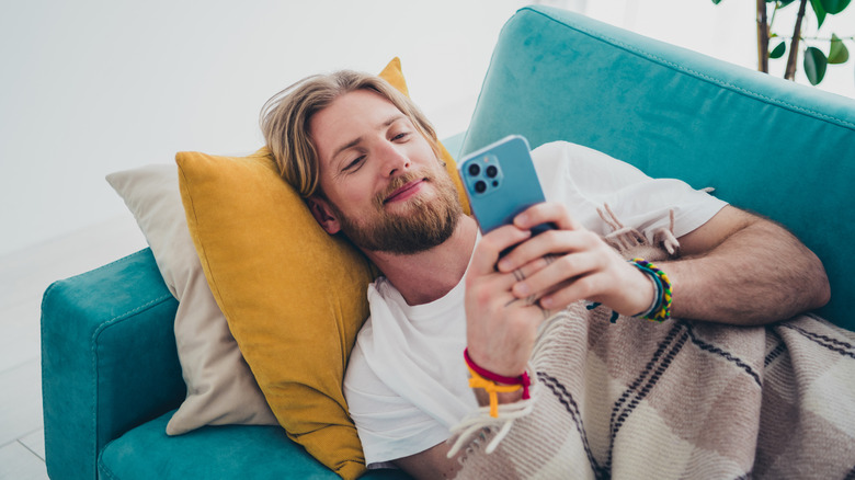 A young man using an iPhone on a sofa