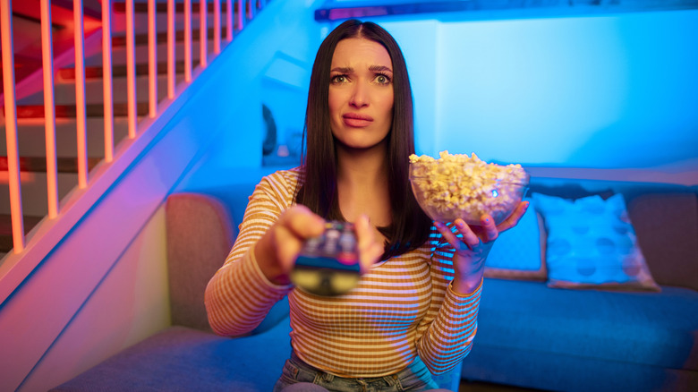 Woman with TV remote and popcorn looking confused and exasperated