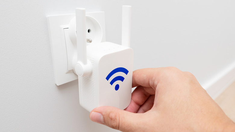 Close-up of a hand plugging a Wi-Fi extender into a wall socket