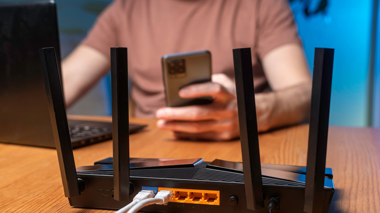 A Wi-Fi router on a desk with a person using a phone and laptop in the background